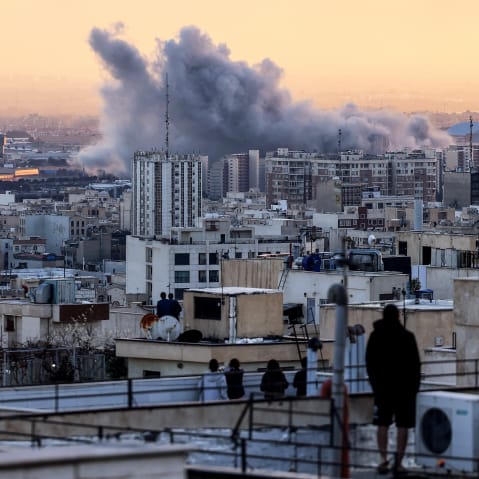 A person stands on the roof of a building looking at a plume of smoke after a strike on March 3, 2026 in Tehran.
