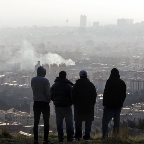 Men watch from a hillside as a plume of smoke rises after an explosion on March 2, 2026 in Tehran.