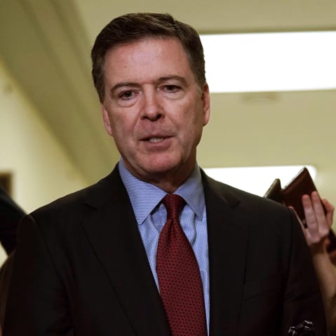 James Comey surrounded by media members holding out cell phones.