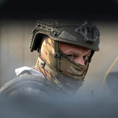 A federal police officer wearing a camouflage face covering is seen behind a chainlink fence.