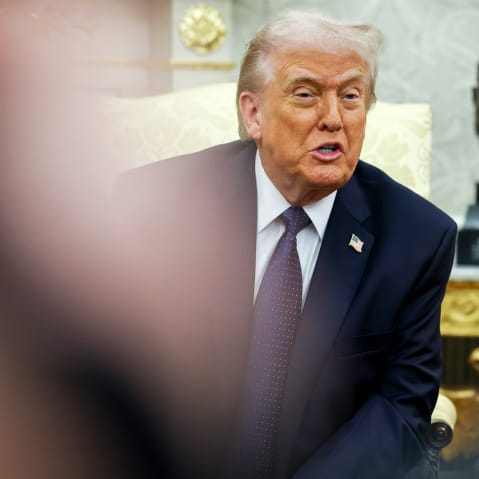 Donald Trump is seen among other people while sitting and speaking in the Oval Office.