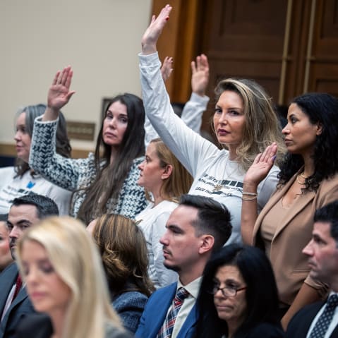 People in focus in the background raise their hands; Pam Bondi out of focus in the foreground looks down.