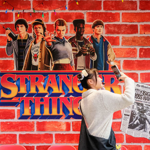 A person takes a photo by a wall embellished with Stranger Things decor.
