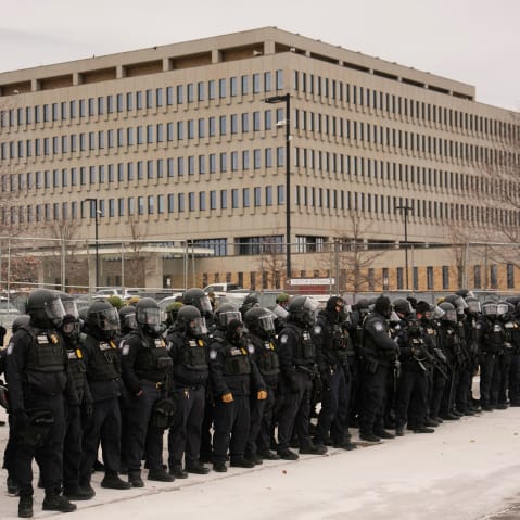 A crowd of federal immigration officers in helmets stand outside the Whipple Federal Building.
