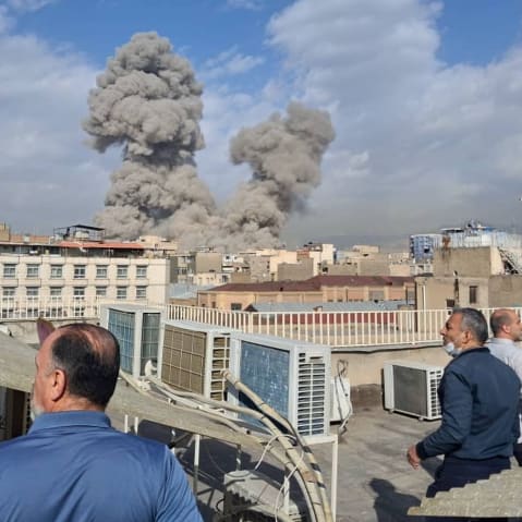 Men standing on rooftops look on at clouds of smoke rise from US airstrikes