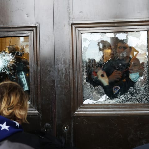 Police officer looks through a broken glass window as protesters stand outside.