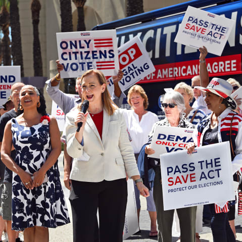 People hold signs saying "Only Citizens Vote" and "Pass the SAVE Act" outside.