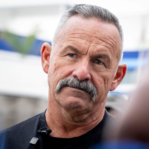 Chad Bianco looks on as he listens to another person.