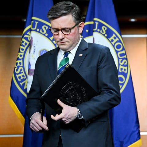 Mike Johnson holds a folder as he walks off the podium.