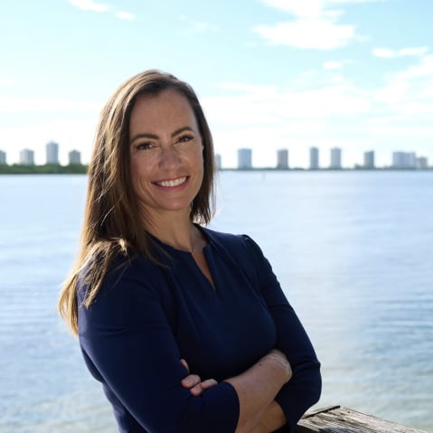 Emily Gregory poses for a photo with her arms crossed in front of her standing in front of a body of water.