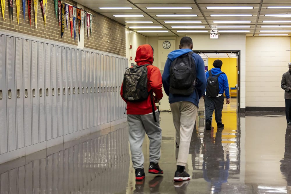 Three students seen from behind as they walk down a high school hallway.