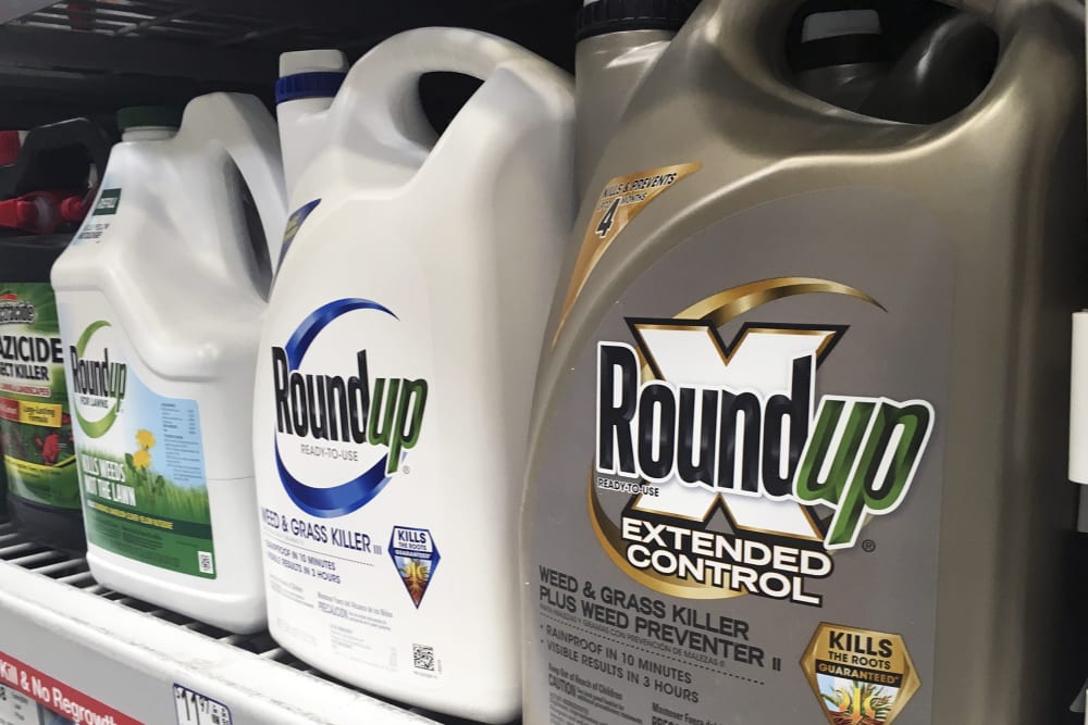 Three Roundup weedkiller bottles sit on a store shelf in this very closeup shot.
