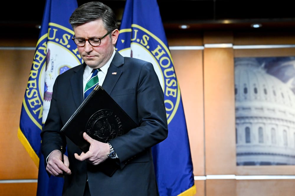 Mike Johnson holds a folder as he walks off the podium.