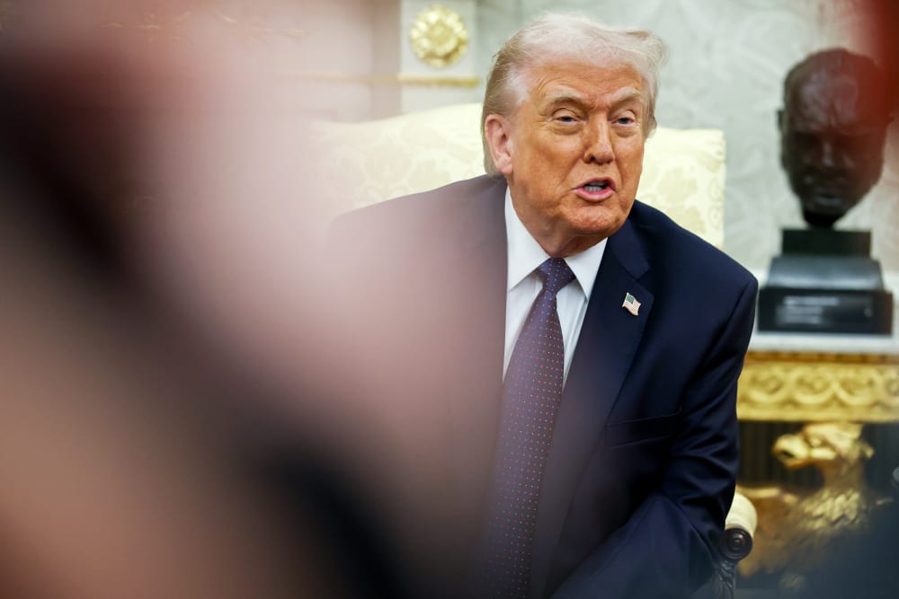 Donald Trump is seen among other people while sitting and speaking in the Oval Office.