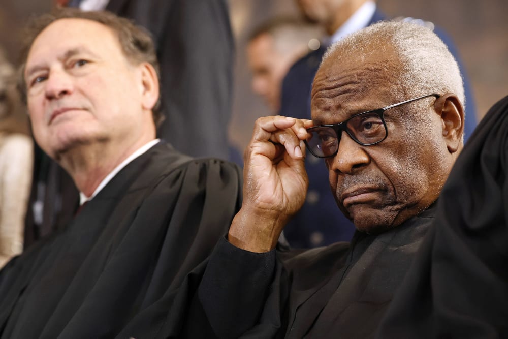 Clarence Thomas adjusts his glasses as Samuel Alito leans back in the background.
