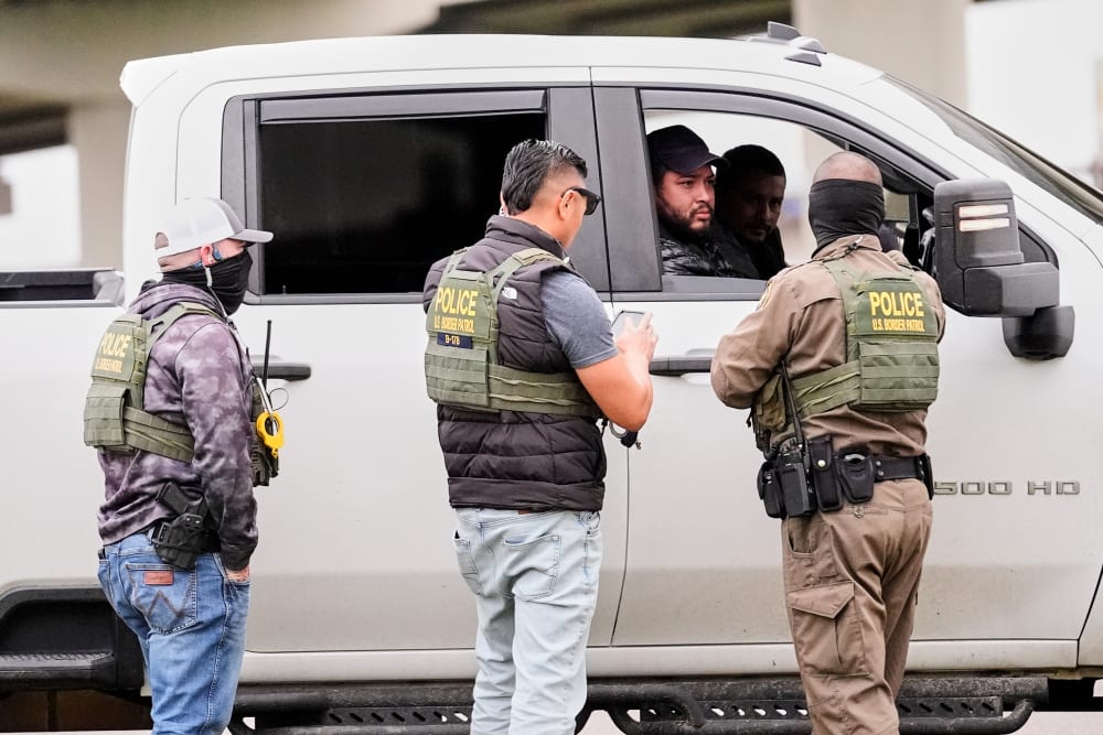 Three federal agents talk to two men in a white truck.