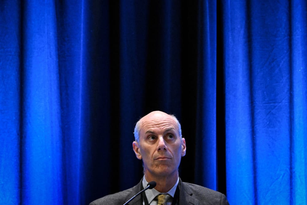 James Boasberg looks up in front of a plain blue background.
