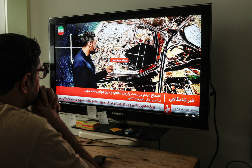 A man is seen from behind watching TV inside a home.