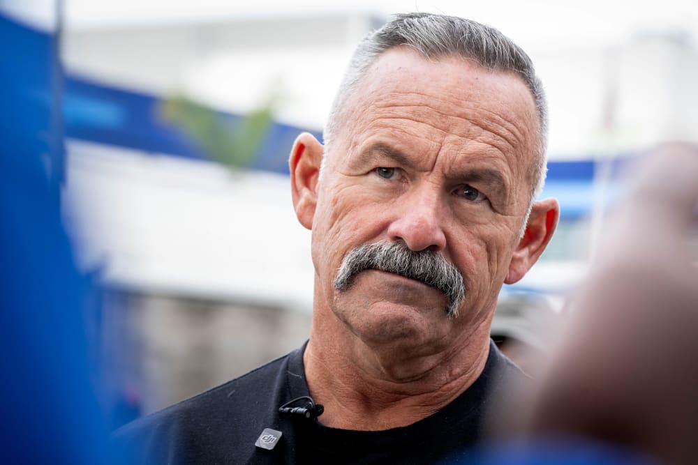 Chad Bianco looks on as he listens to another person.