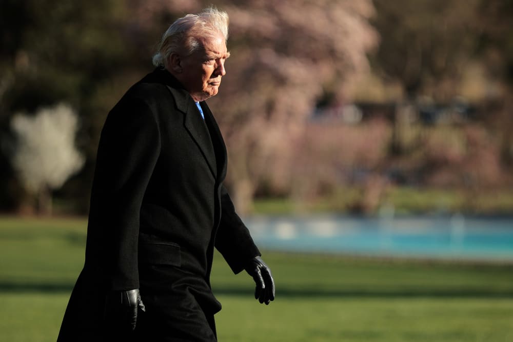 Donald Trump walks at sunset toward the White House building.