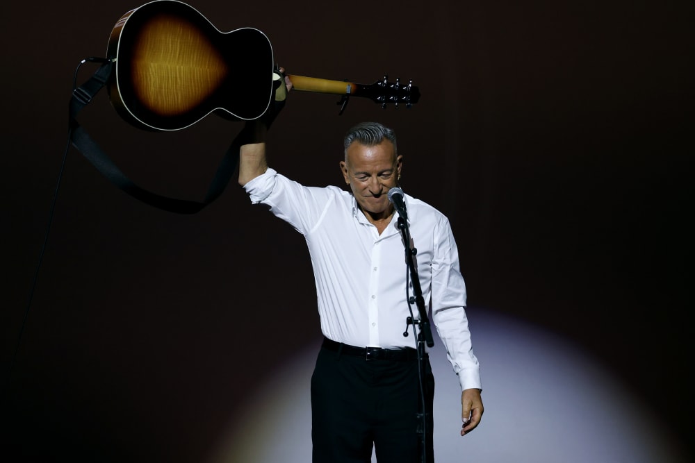 Bruce Springsteen holds a guitar above his head.