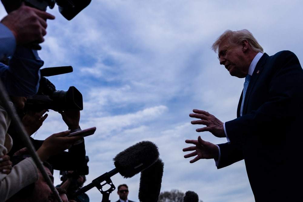 In this photo shot from below, journalists with mics and recorders can be seen on the left as Donald Trump speaks to them as he makes a gesture with his hands.
