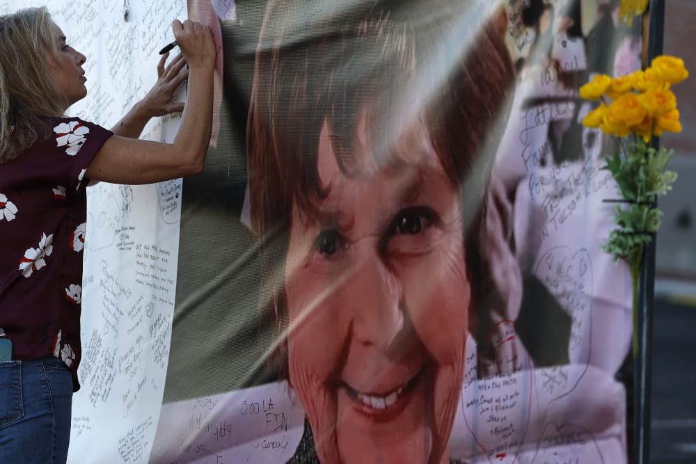 A woman on the left writes on a banner that has Nancy Guthrie's picture on the right.