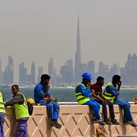 Workers sit on a wall against the Dubai backdrop of the city skyline as they take a break.