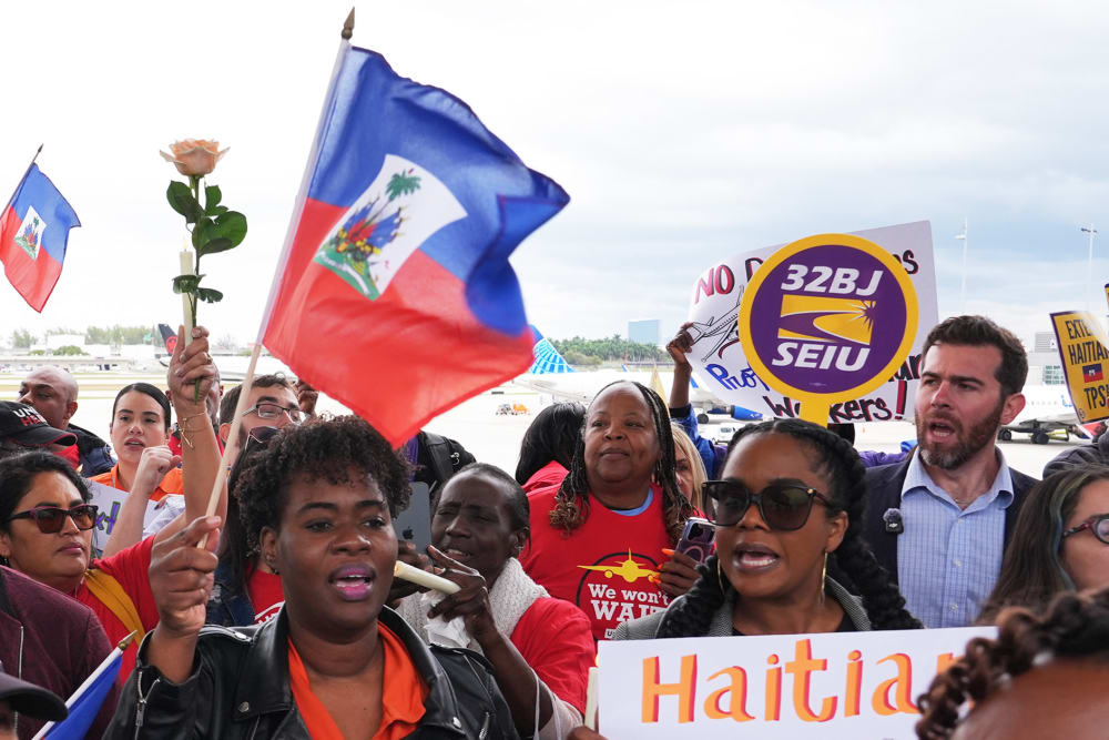 A crowd of people wave Haitian flags and hold signs calling for an extension to Haitian TPS.