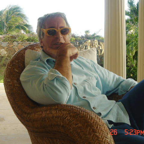 Jeffrey Epstein sits at a patio wearing yellow framed sunglasses.