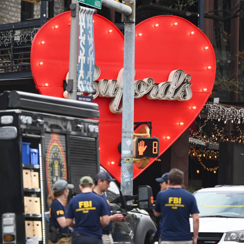 People wearing shirts that say "FBI" stand by an FBI truck outside of a bar. The front entrance of the bar is decorated with a big red heart that has the name "Buford's" in cursive in the center.