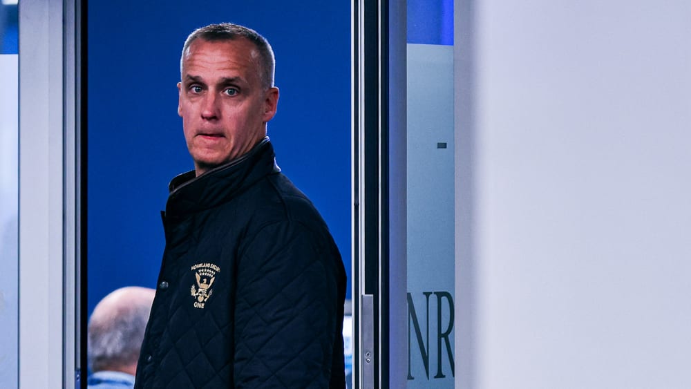 Corey Lewandowski stands in a doorway. Blurred in the foreground, people work at their desks.