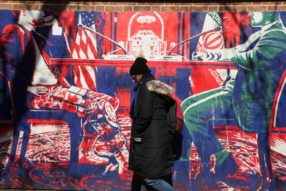 A woman walks by a red and blue mural that sends an anti-american message.