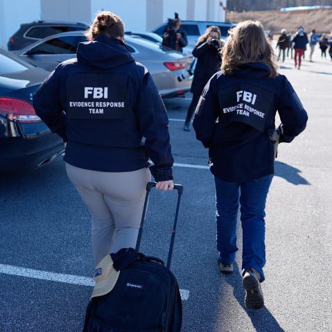 Two FBI agents walk in a parking lot, one dragging a bag.