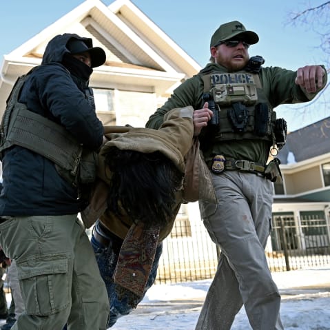 Multiple federal agents drag two people by the arms.