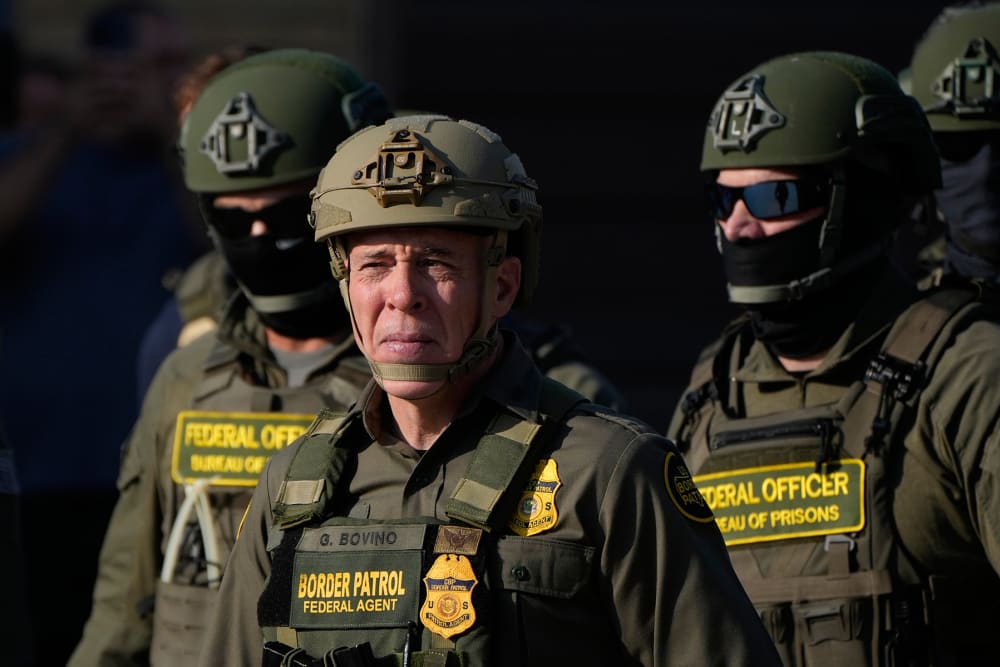 Greg Bovino, center, squints in the light beside multiple federal immigration agents.