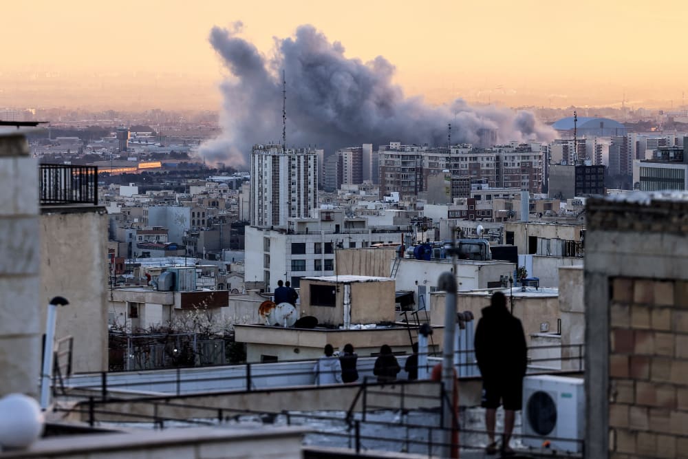 A person stands on the roof of a building looking at a plume of smoke after a strike on March 3, 2026 in Tehran.