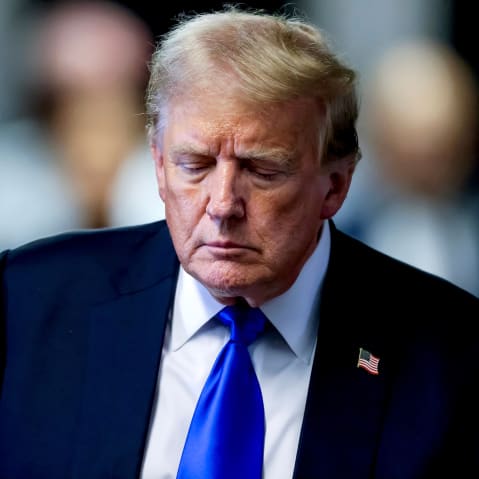 Donald Trump walks down the hallway, looking down, in a closeup photograph.