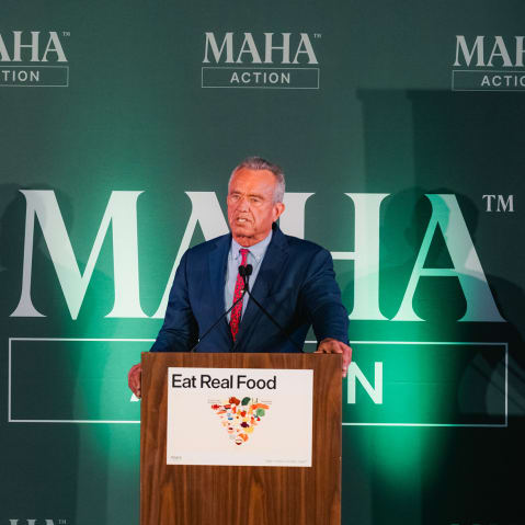 RFK Jr. stands behind a podium that has a sign featuring his updated food pyramid.