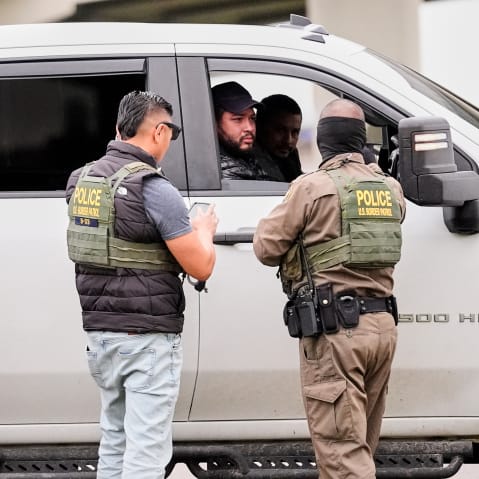 Three federal agents talk to two men in a white truck.