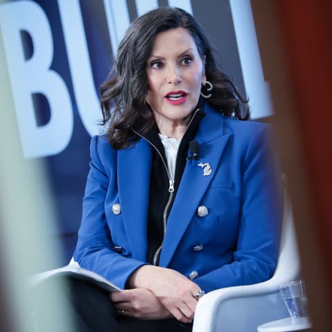 Gretchen Whitmer sits at the stage, seen through two lines.