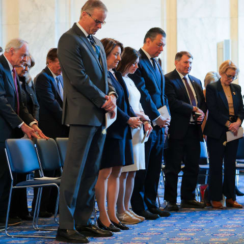 While standing, people bow their heads and hold their hands together.