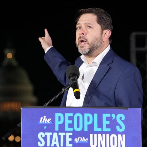 Ruben Gallego points at the capitol building as he speaks outside at night.