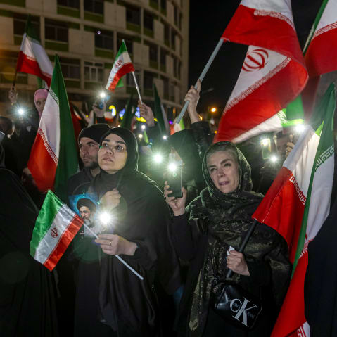 A crowd of people hold pictures of Ayatollah Ali Khamenei and wave Iranian flags.