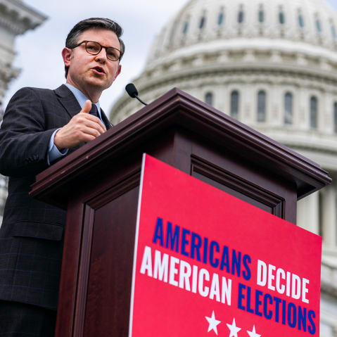 Mike Johnson, right, and Rep. Chip Roy at a podium in front of the Capitol. The podium has a red sign that says "Americans decide American elections."