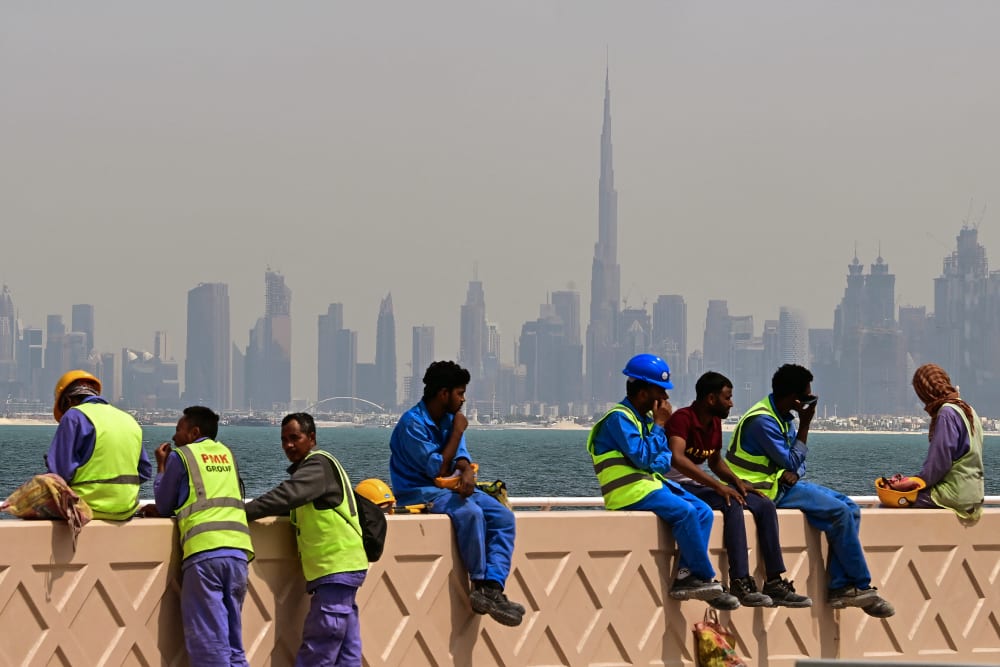 Workers sit on a wall against the Dubai backdrop of the city skyline as they take a break.
