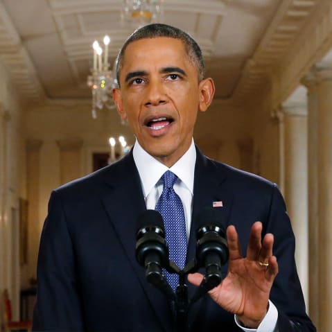 Barack Obama gestures behind a podium and microphone.