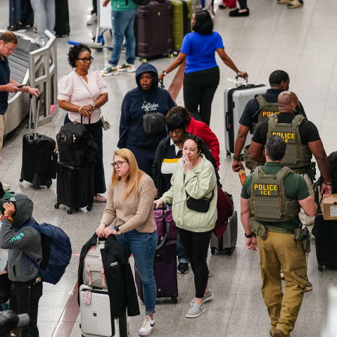 People wait in line at the baggage claim area as three ICE agents walk around.