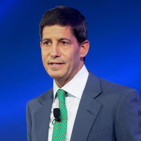 Kevin Warsh seen at the podium with a blue background.