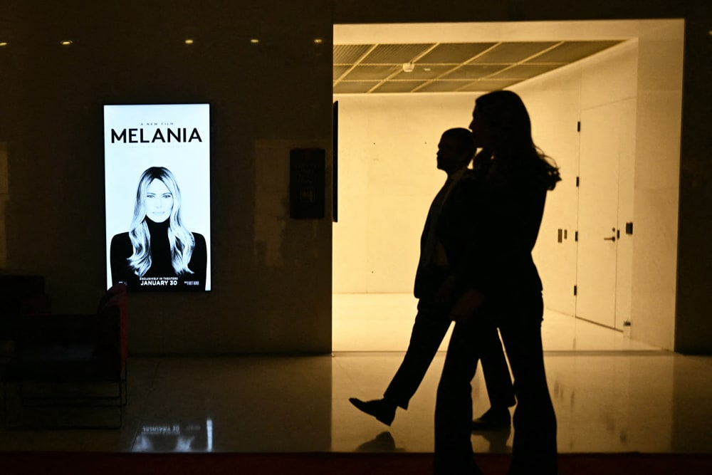 Silhouettes walk past a poster for "Melania."